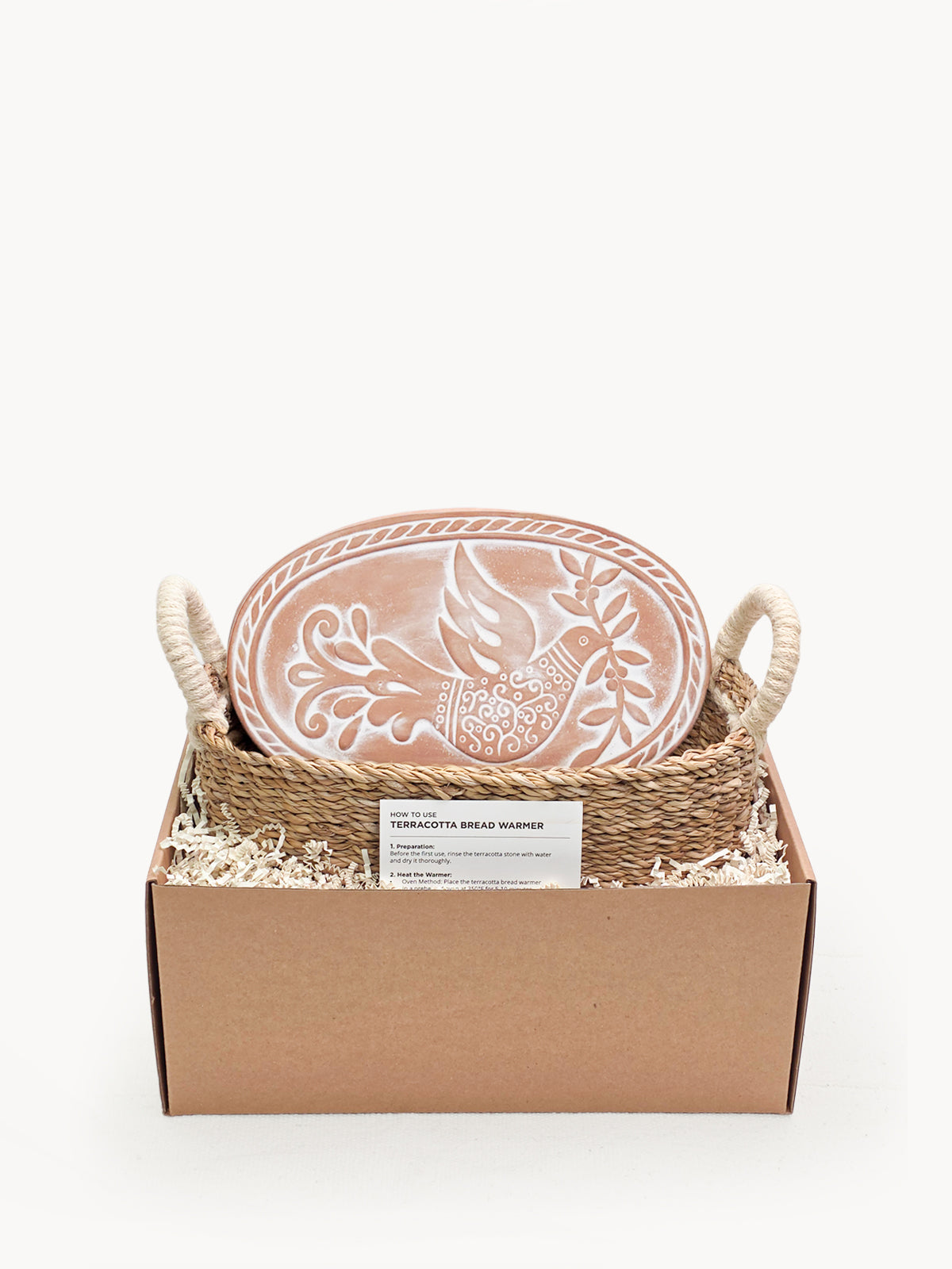 Terracotta bread warming stone with bird engraving resting inside a handwoven seagrass basket.