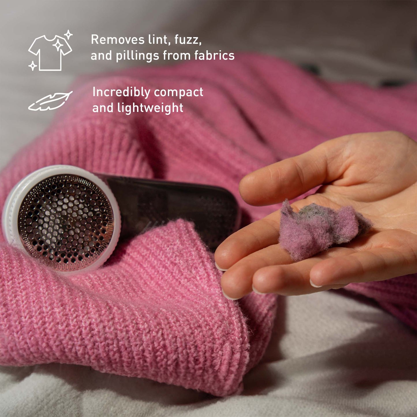 Pursonic cordless lint remover shaving fuzz and lint from a sweater, showing collected fabric pills in hand.