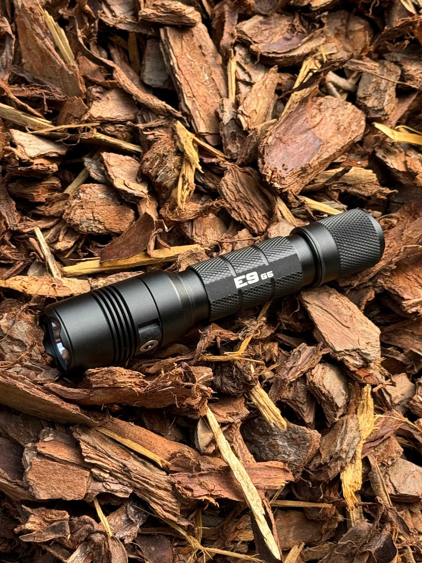 Powertac E9 GEN5 tactical flashlight on forest ground for hiking, camping, and survival use