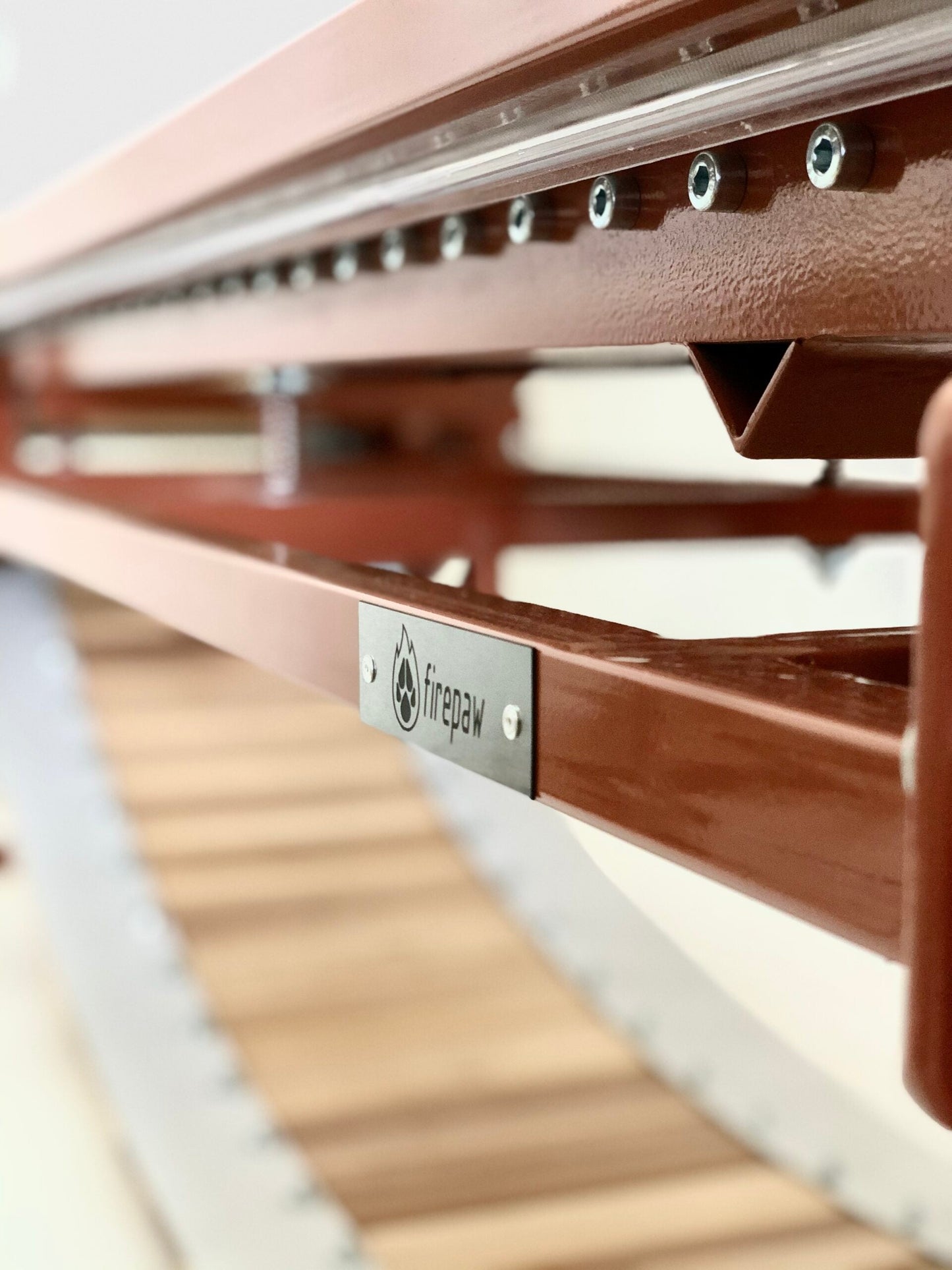A high-angle close-up of a FirePaw professional dog treadmill, showcasing the durable brown-painted steel frame, precision bolts, and the natural wooden running slats.