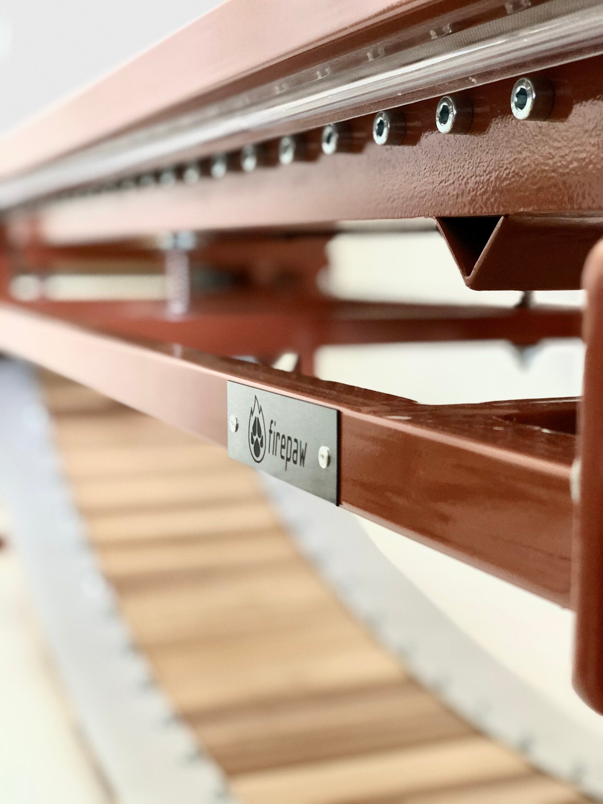 A high-angle close-up of a FirePaw professional dog treadmill, showcasing the durable brown-painted steel frame, precision bolts, and the natural wooden running slats.