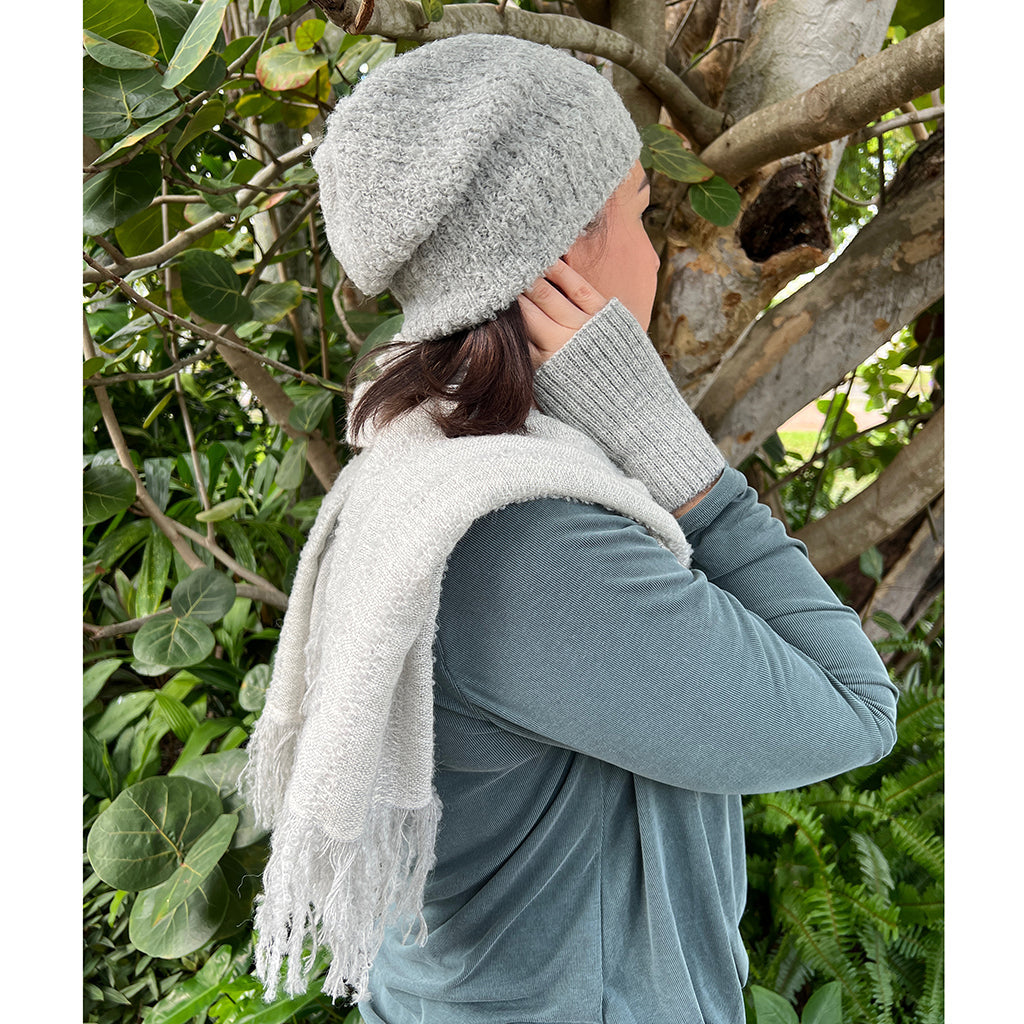 Person wearing a gray knit hat and scarf in a natural setting with greenery.