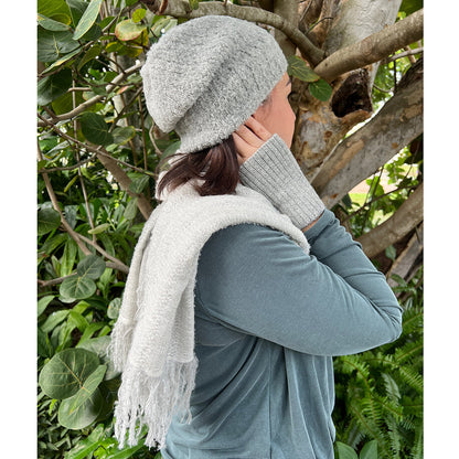 Person wearing a gray knit hat and scarf in a natural setting with greenery.