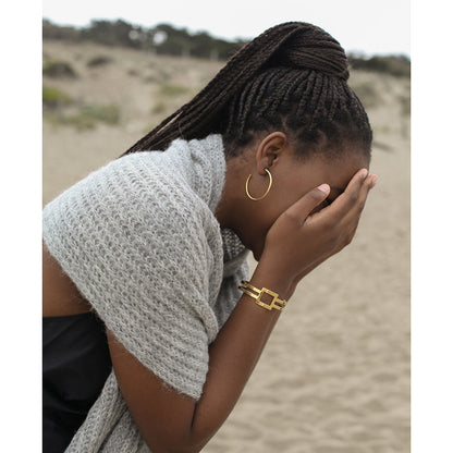 Woman on a beach wearing a gray knit scarf.