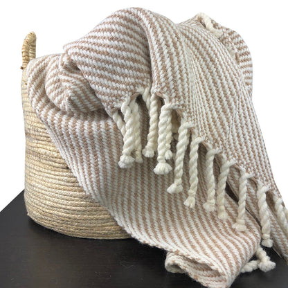 Beige and brown striped blanket with tassels draped over a woven basket on a black surface.