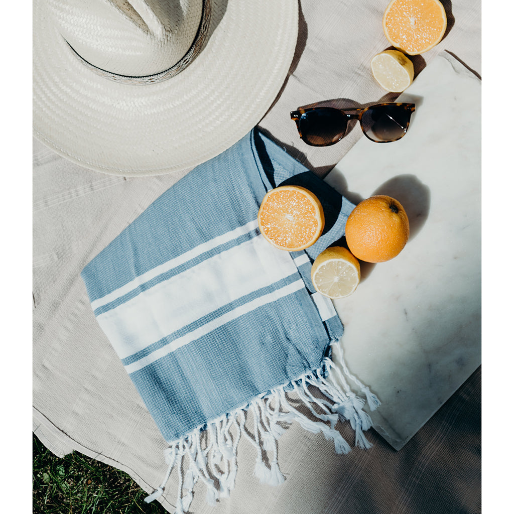 Towel with white stripes on a marble surface with oranges and sunglasses.
