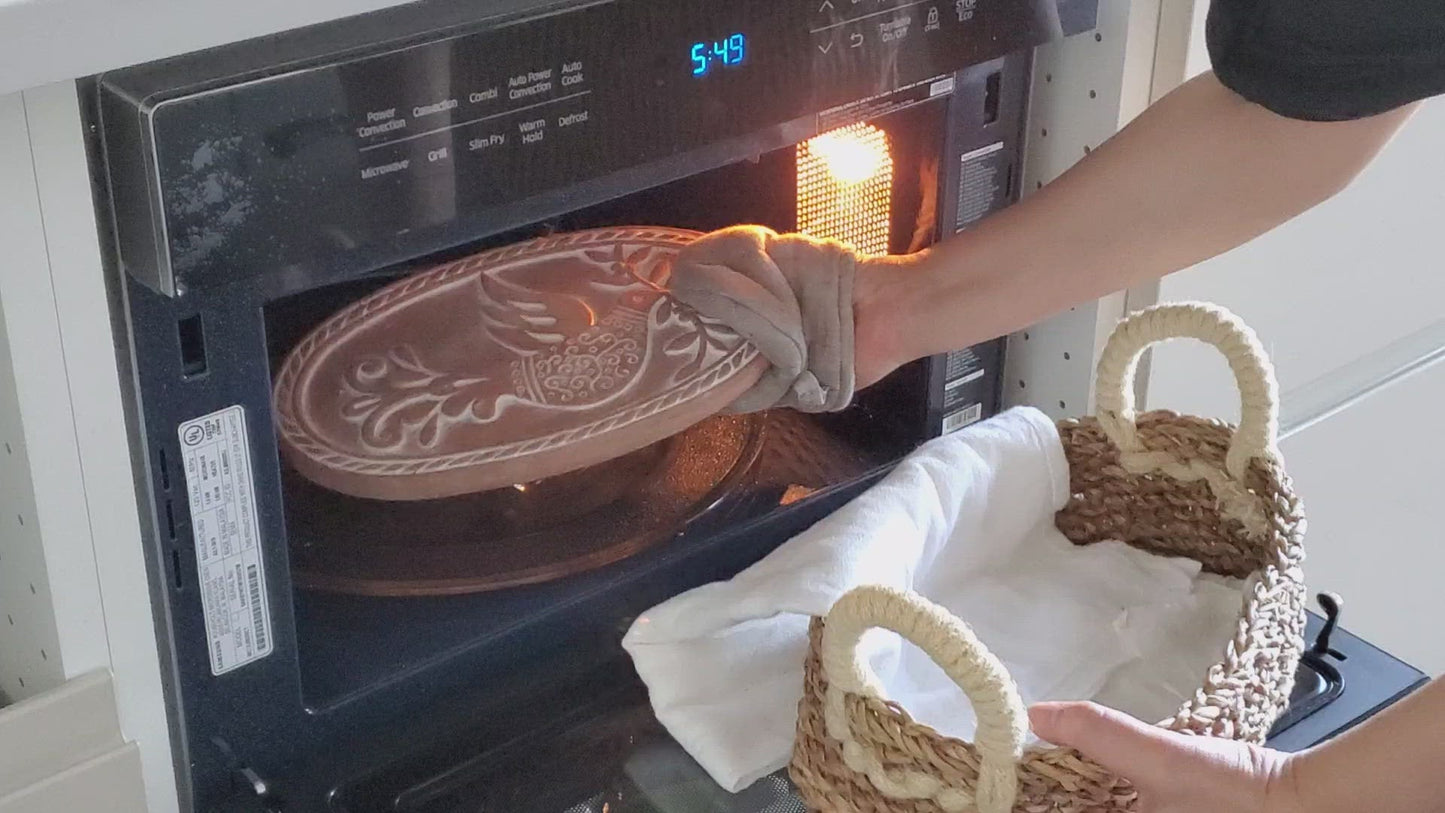 Removing a heated terracotta bread warming stone from the oven with an oven mitt.