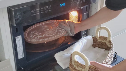Removing a heated terracotta bread warming stone from the oven with an oven mitt.