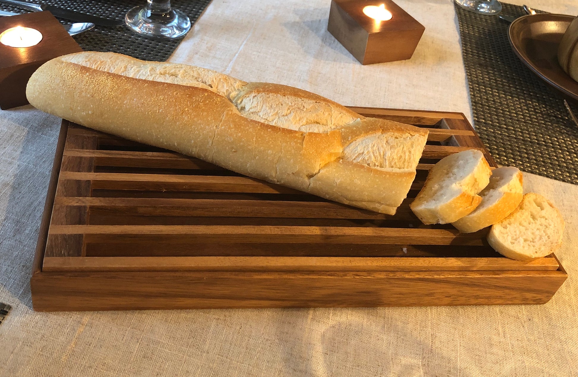 Sliced baguette served on a wooden crumb catcher tray on a dining table with candles.