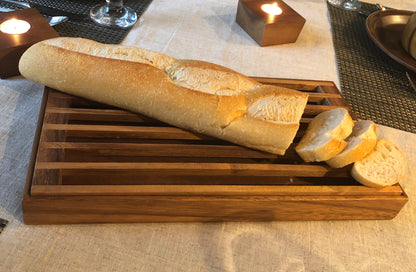Sliced baguette served on a wooden crumb catcher tray on a dining table with candles.