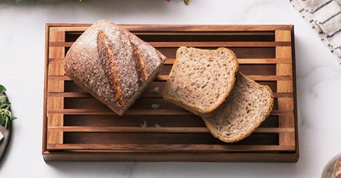 Overhead view of sliced bread on an acacia wood crumb catcher tray with crumbs falling through the slats.