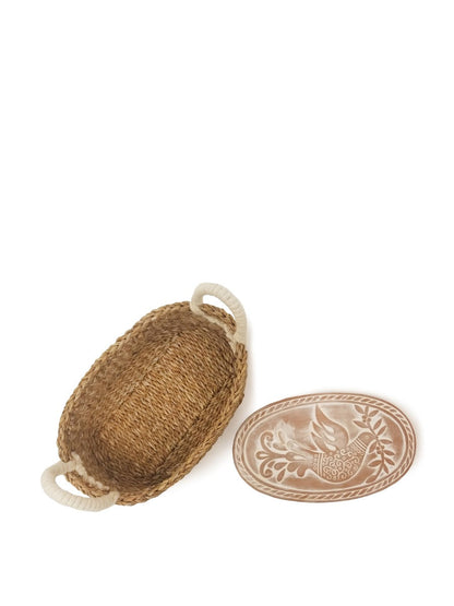 Top-down view of an oval seagrass bread basket with engraved terracotta warming stone.