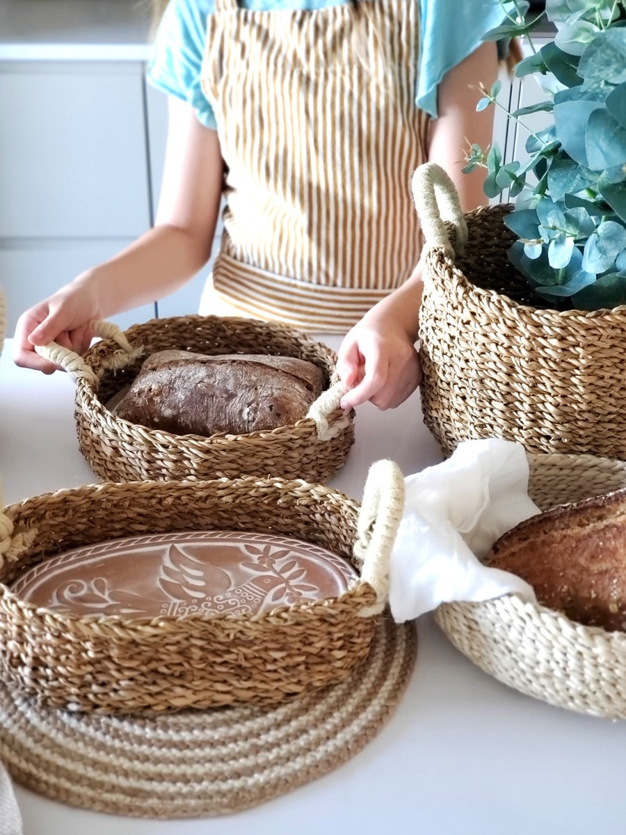 Fresh artisan bread being served in a woven seagrass basket with terracotta bread warmer.