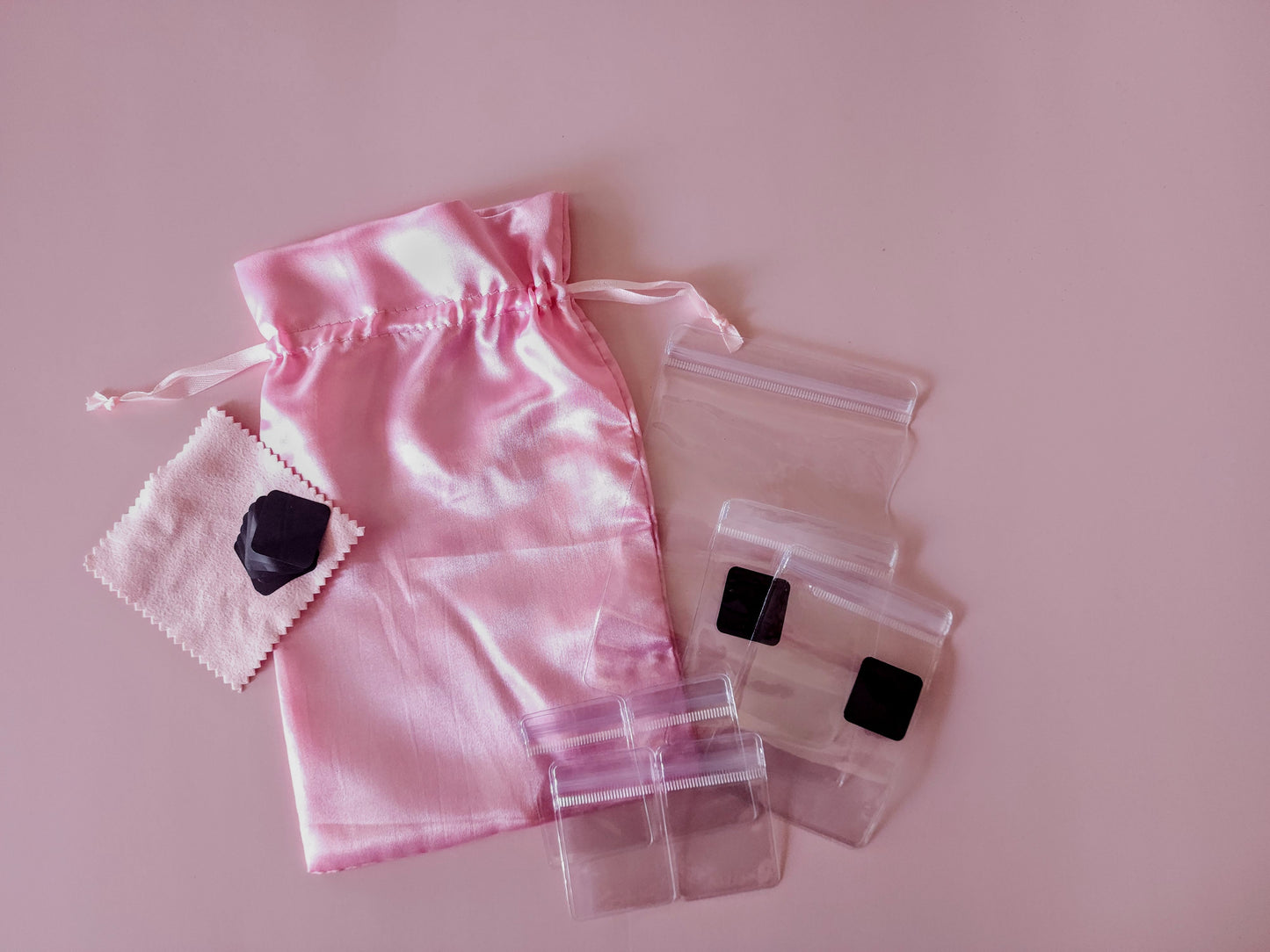 Pink satin jewelry travel organizer set with multiple soft pouches and clear zip cases laid out flat
