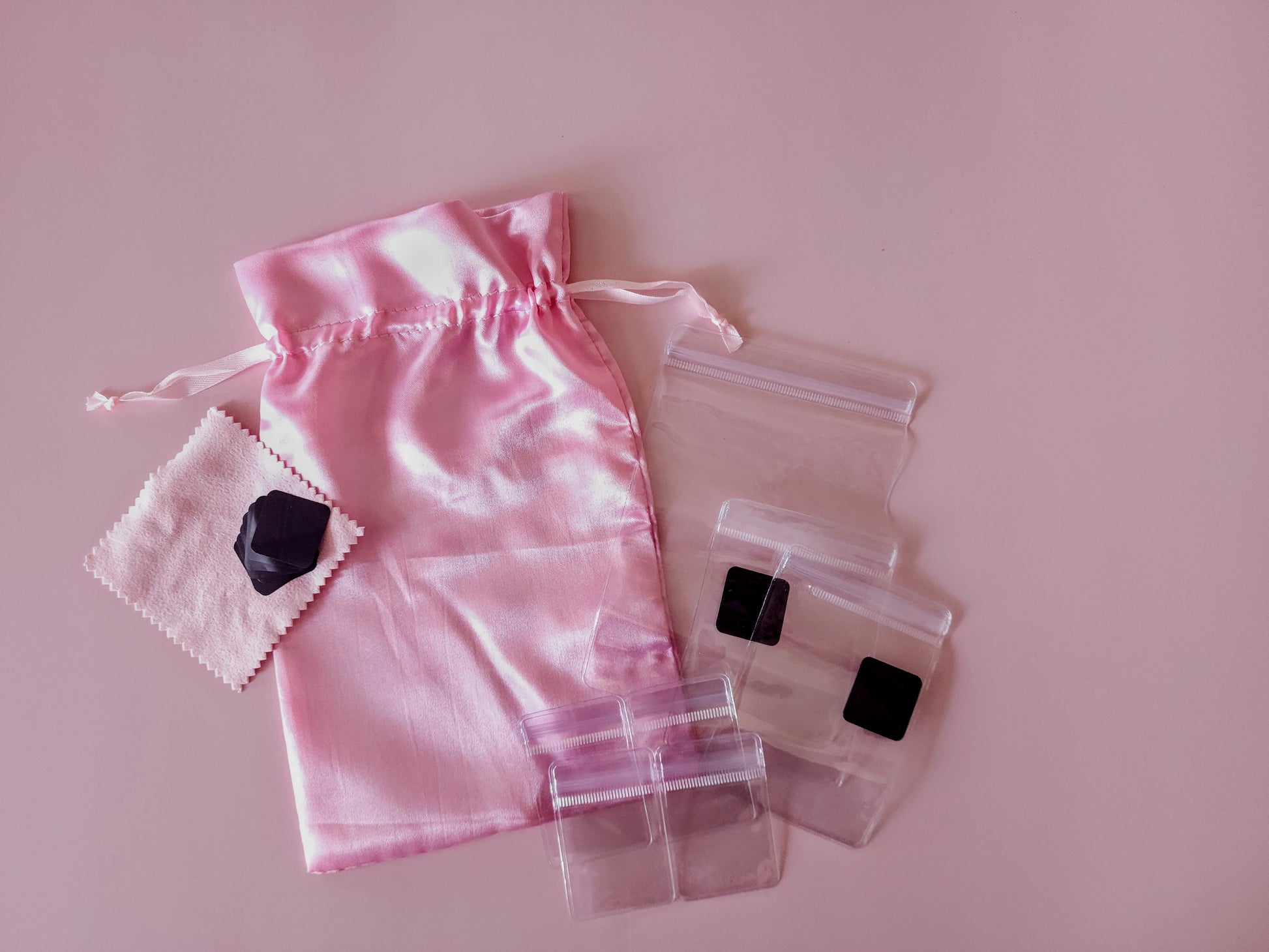 Pink satin jewelry travel organizer set with multiple soft pouches and clear zip cases laid out flat
