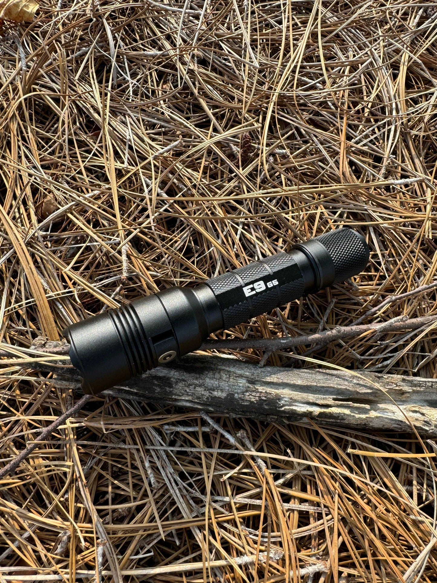 Powertac E9 GEN5 tactical flashlight outdoors on forest ground, designed for camping, hiking, and emergency use