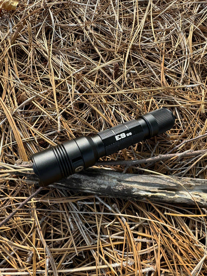 Powertac E9 GEN5 tactical flashlight outdoors on forest ground, designed for camping, hiking, and emergency use