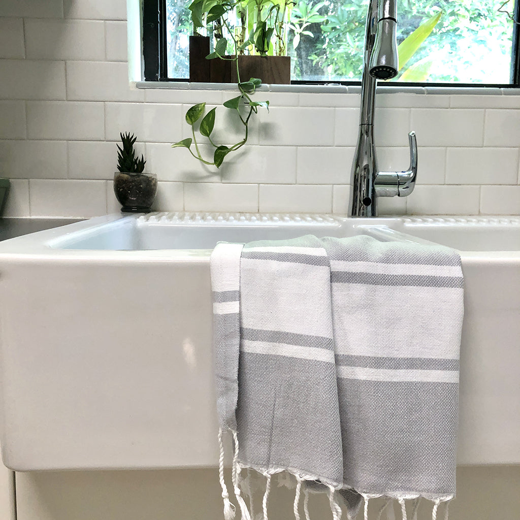 Towel draped over a white kitchen sink with a tiled wall and plants in the background.